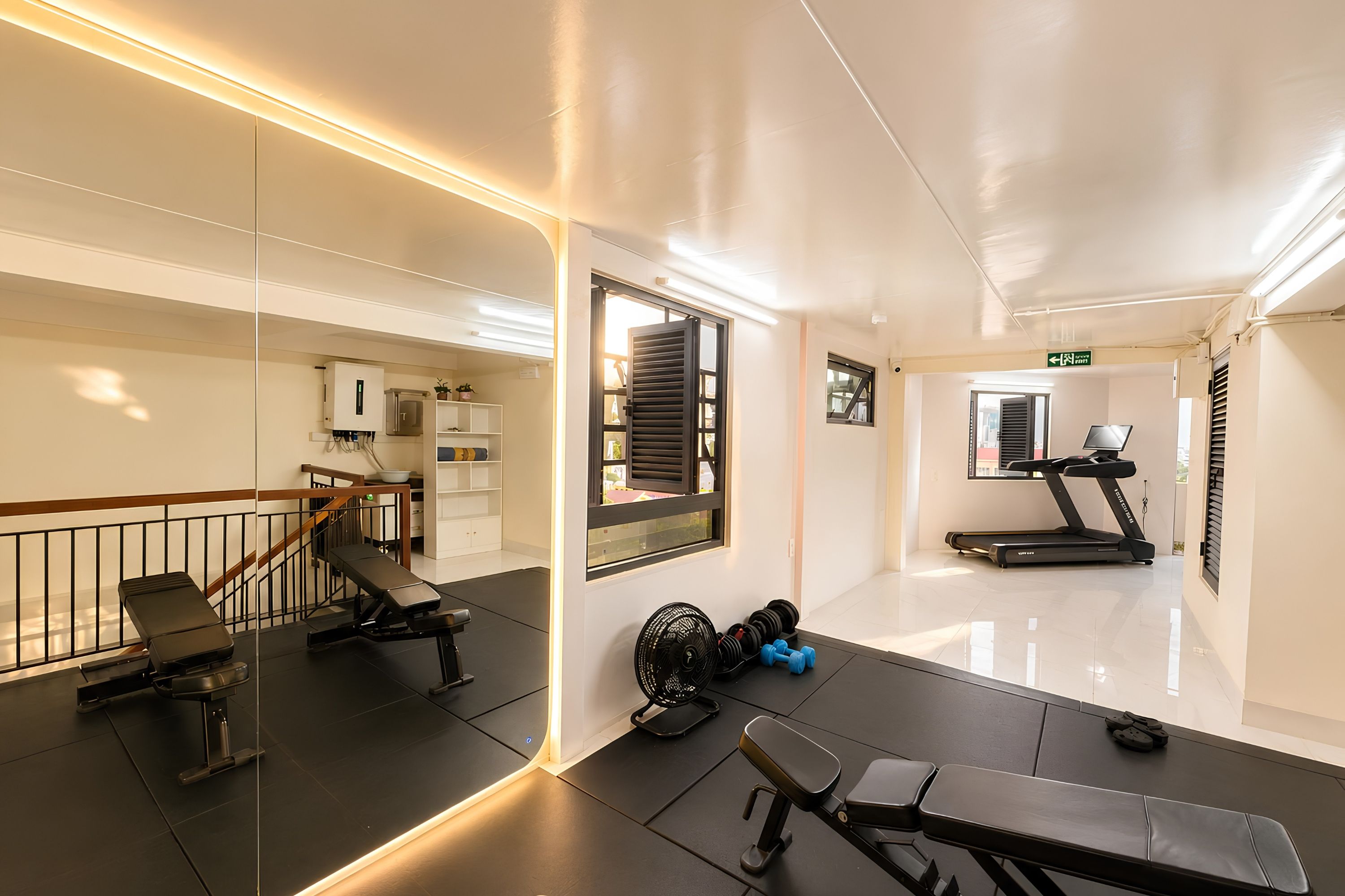 A gym with exercise equipment, a treadmill, and a mirror reflecting the space.