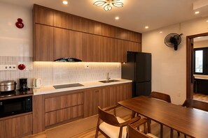 A modern kitchen with wooden cabinets, a built-in oven, a sink, and a dining area with a table and chairs. - MT Danang Hotel - Near Dragon Bridge (An Hai)