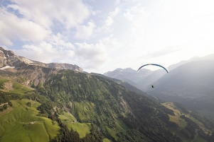 Paisaje montañoso con una persona practicando parapente.