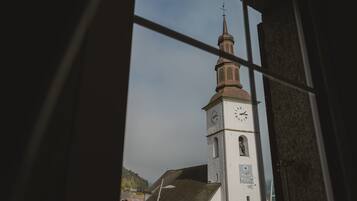 Ett kyrktorn med en klocka och en vindflöjel, sett genom ett fönster med ett rutmönster.