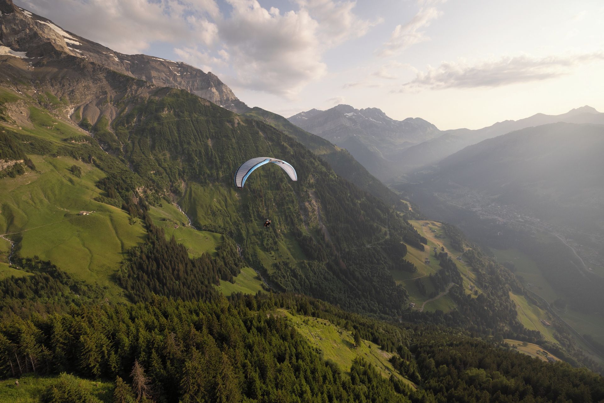 Paisaje montañoso con una persona practicando parapente.