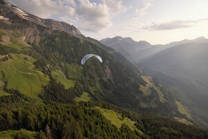 Paisaje montañoso con una persona practicando parapente.