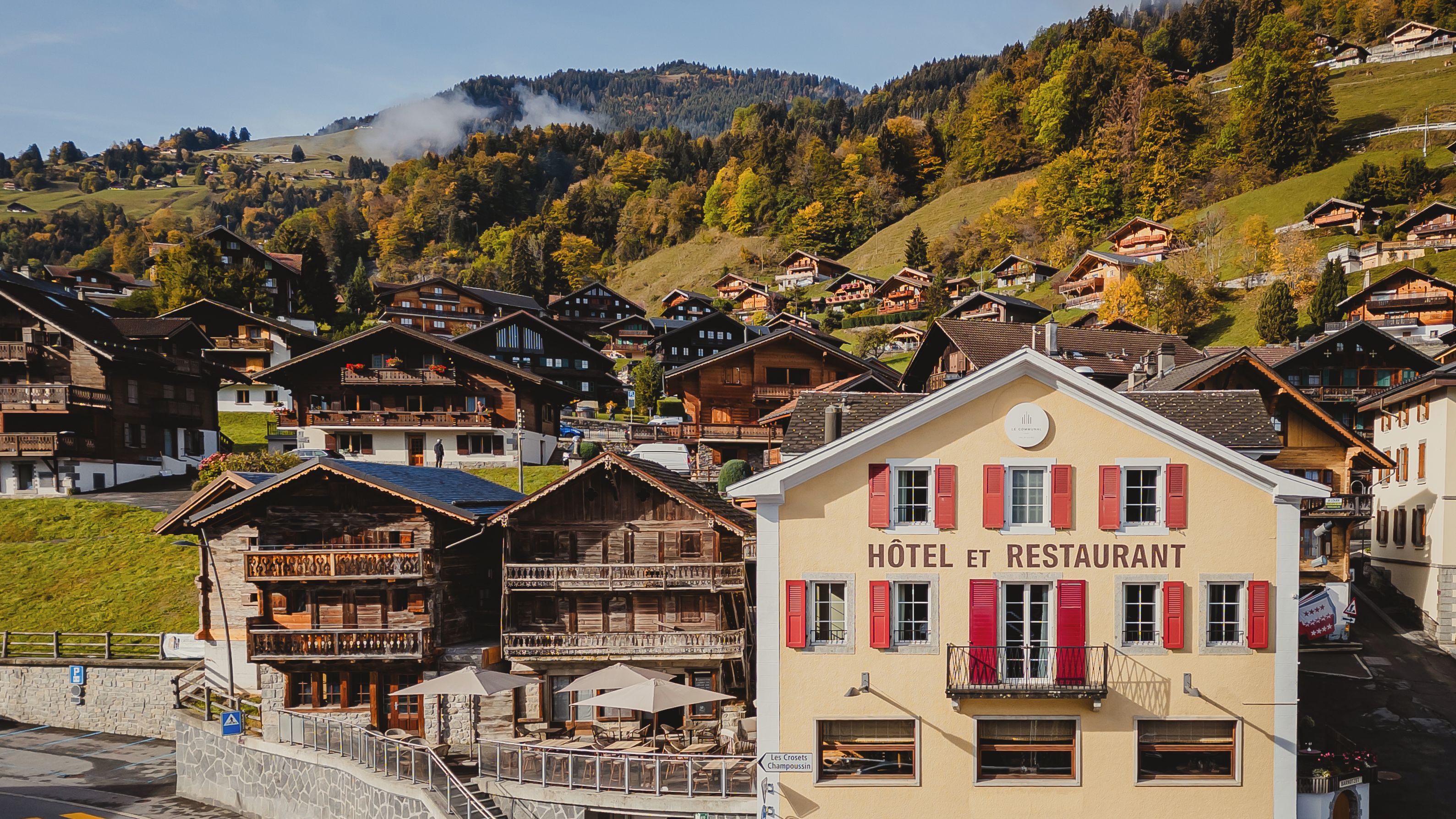 Un hôtel avec une enseigne indiquant « HÔTEL ET RESTAURANT » et une vue sur une colline parsemée de maisons.