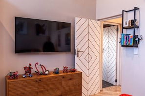 Ein Zimmer mit einem an der Wand befestigten Fernseher, einem Holzschrank mit Spielzeug, einer verzierten Tür und einem Bücherregal mit Büchern.