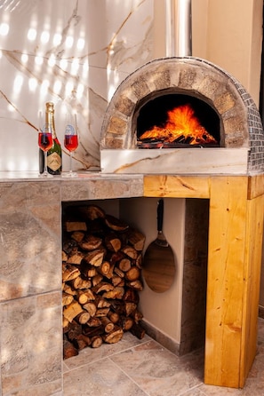 Ein Steinkamin mit Feuer, einem Holzstoß und zwei Gläsern Rotwein.
