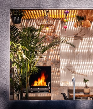 A fireplace with a fire, a hanging plant, and a table with chairs.