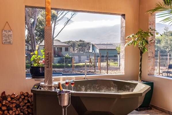 A room with a large bathtub, a window with a view of houses, a sign on the wall, and a potted plant.