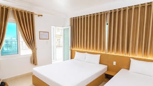 A hotel room with a large bed, a smaller bed, a window with curtains, and a view of buildings outside. - Cat Ba Thai Long Hotel (Cat Hai)