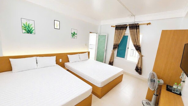 A hotel room with two beds, a desk with a fan, and a window with curtains. - Cat Ba Thai Long Hotel (Cat Hai)