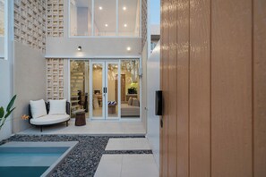 A modern outdoor living area with a pool, seating, and a wooden door. - Tranquil 24 Villa by Betterplace (Pecatu)