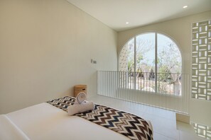 Ein Schlafzimmer mit einem großen Bogenfenster, einem Bett mit gemustertem Überwurf und einem kleinen gewebten Korb.