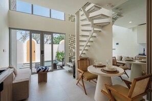 A modern interior with a spiral staircase, a dining area with a round table, and a view of the outdoors through glass doors. - Tranquil 24 Villa by Betterplace (Pecatu)