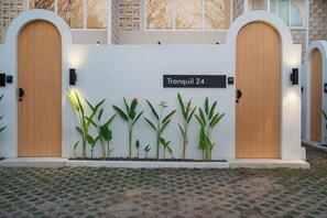 Ein Gebäudeeingang mit zwei Holztüren, einem Schild mit der Aufschrift 'Tranquil 24' und einer Reihe Pflanzen davor.