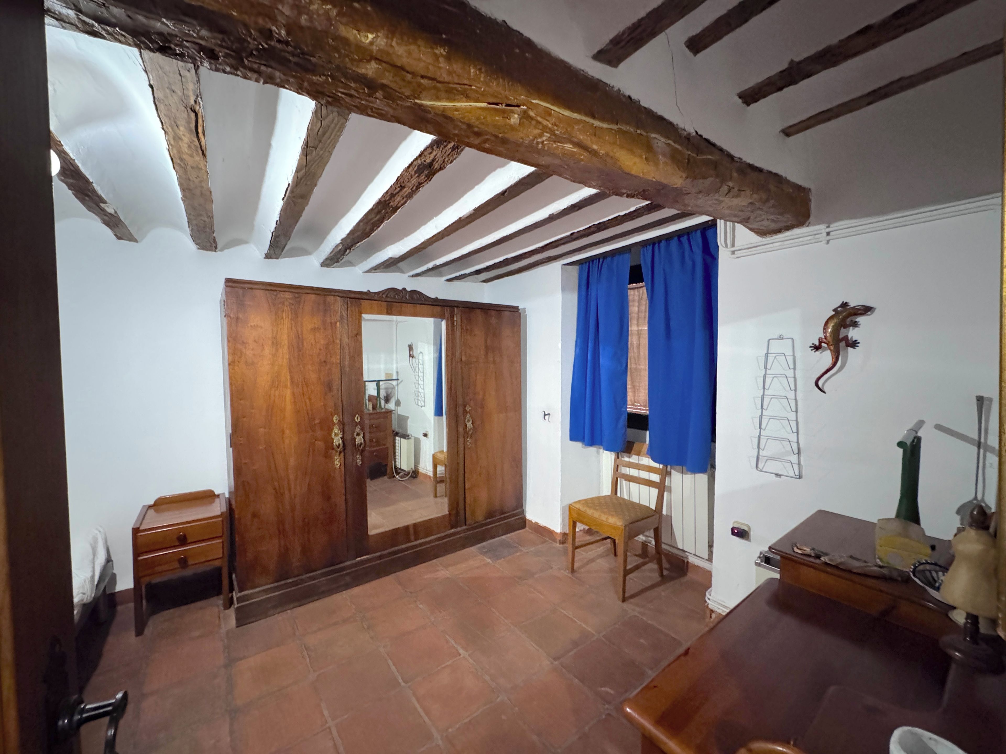 Une pièce avec une armoire en bois, une chaise, une table et un plafond avec des poutres apparentes.