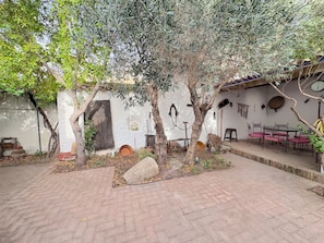 Un patio con piso de ladrillo, una mesa con sillas y una pared rústica con varios objetos.