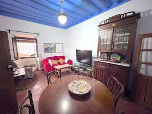 Een eetgedeelte met een houten tafel, stoelen, een rode bank, een televisie en een kast met glazen deuren.
