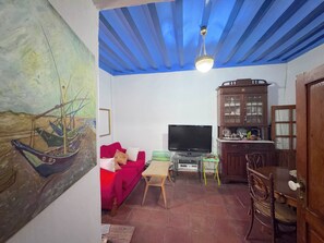Ein Wohnzimmer mit einem roten Sofa, einem Fernseher, einem Holzschrank und einer Decke mit blauen Balken.