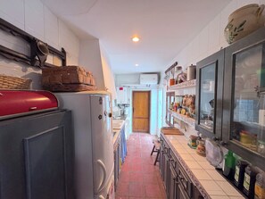 A narrow kitchen with a refrigerator, a microwave, and a sink. There is a wooden door leading to another room.