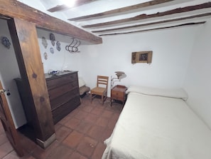 A bedroom with a wooden dresser, a chair, a desk with a lamp, and a bed.