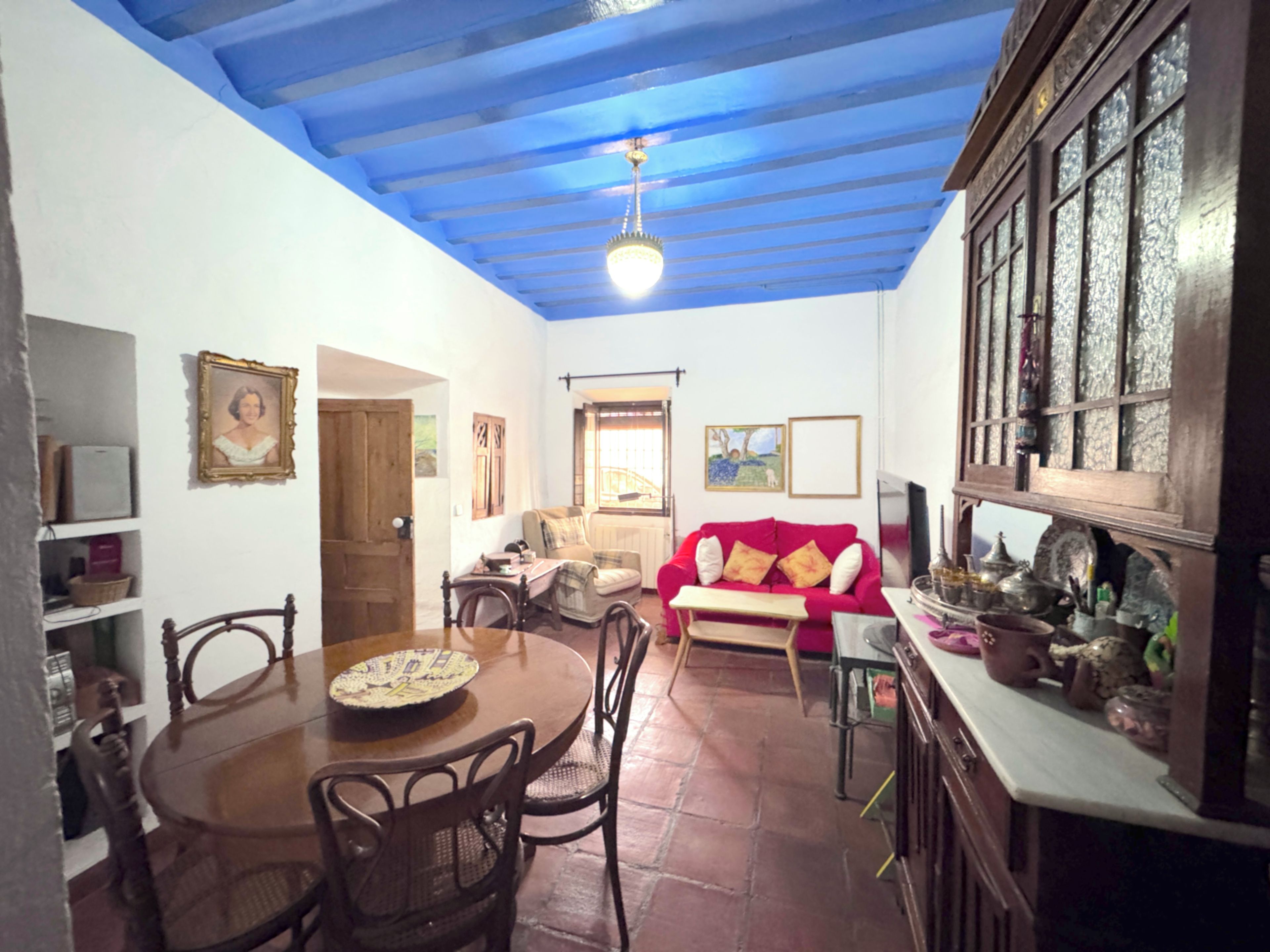 Un comedor con mesa y sillas de madera, un sofá rojo y una zona de cocina con armarios y una estufa.