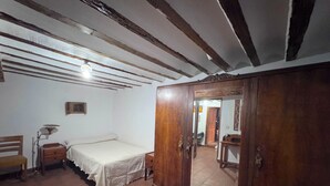 Una habitación con cama, un armario de madera, un escritorio con lámpara y una silla.