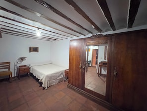 Ein Zimmer mit einem Bett, einem Holzschrank, einem Schreibtisch mit Lampe und einem Stuhl.