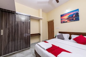 A hotel room with a bed, a wardrobe, a painting on the wall, and a door leading to another room.