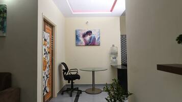 A hallway with a ceiling light, a painting, a water dispenser, a chair, and a small table.
