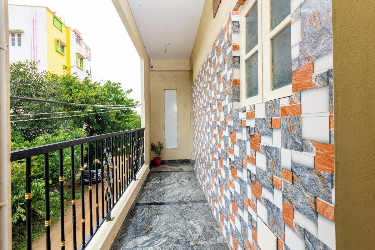 Un balcon étroit doté d’une rambarde en métal noir, d’un pot de fleurs et d’un mur recouvert de carreaux formant un motif géométrique.