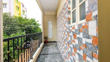 A narrow balcony with a black metal railing, a potted plant, and a tiled wall with a geometric pattern.
