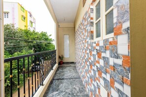 A narrow balcony with a black metal railing, a potted plant, and a tiled wall with a geometric pattern.