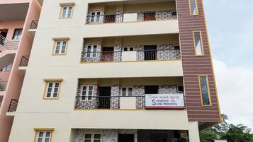 Un edificio de varios pisos con balcones, un letrero que dice 'Symphony Suites Homestay' y un coche estacionado al frente.