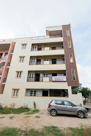 Un edificio de varios pisos con balcones, un letrero que dice 'Symphony Suites Homestay' y un coche estacionado al frente.