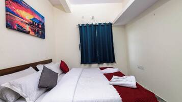 A hotel room with a bed, a red blanket, a painting on the wall, and a window with curtains.