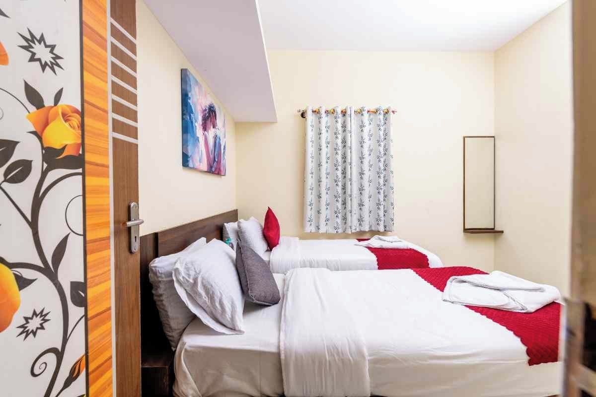 A hotel room with two beds, a painting on the wall, a window with curtains, and a mirror.