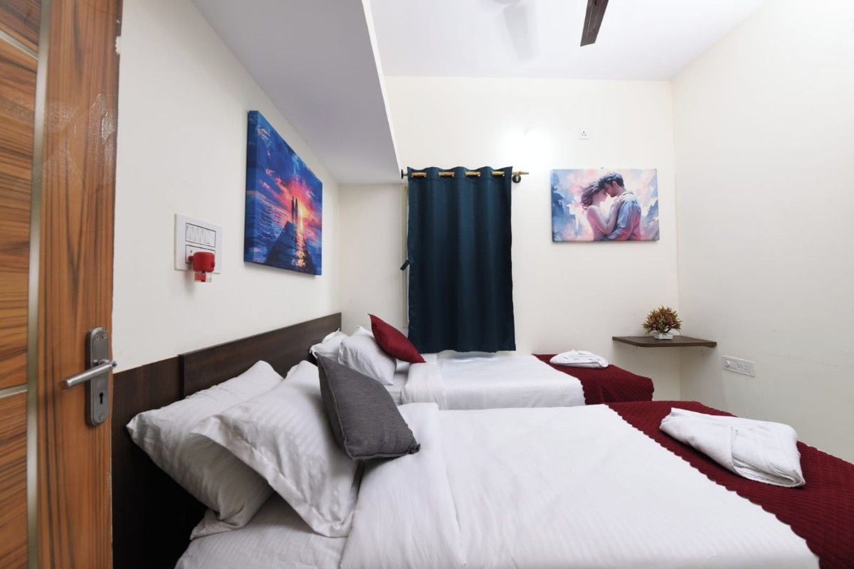 A hotel room with two beds, a red curtain, and artwork on the walls.