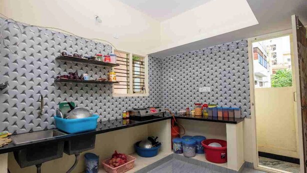 Una cocina compacta con cubierta negra, paneles de pared grises con textura y una ventana.