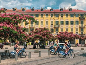 Une rue bordée d’immeubles jaunes, où l’on voit des gens à vélo et des arbres en fleurs aux teintes roses.