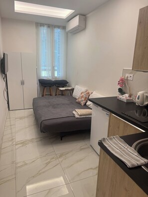 Une pièce de taille modeste comprenant un lit, une petite table, un canapé, un coin cuisine et un téléviseur fixé au mur.