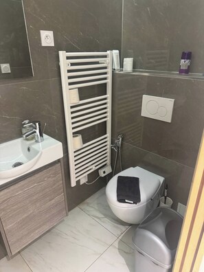 Ein Badezimmer mit einem weißen Waschbecken, einer Toilette, einem Handtuchhalter und einer Duschkabine.