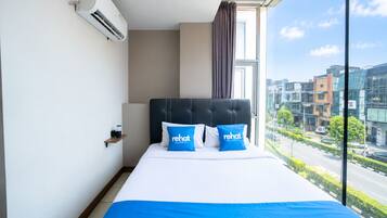 A hotel room with a large bed, a view of the city, and an air conditioning unit on the wall.