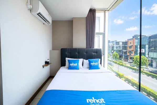 Habitación de hotel con una cama grande, vistas a la ciudad y un equipo de aire acondicionado en la pared.