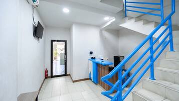 Un vestíbulo de hotel con un mostrador de recepción, una escalera con barandillas azules y un extintor cerca de la entrada.