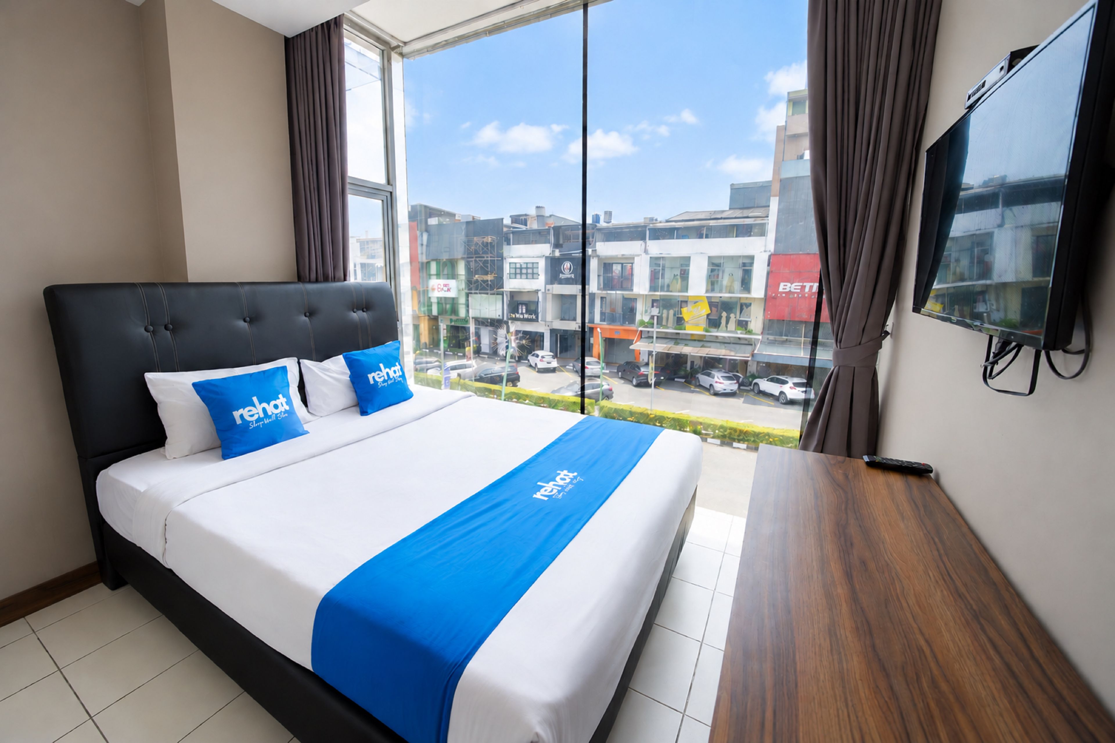 A hotel room with a large bed, a TV on the wall, and a view of the city through the window.