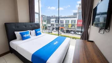 A hotel room with a large bed, a TV on the wall, and a view of the city through the window.