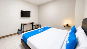 Habitación de hotel con cama, escritorio, televisor montado en la pared y mesita de noche con lámpara.