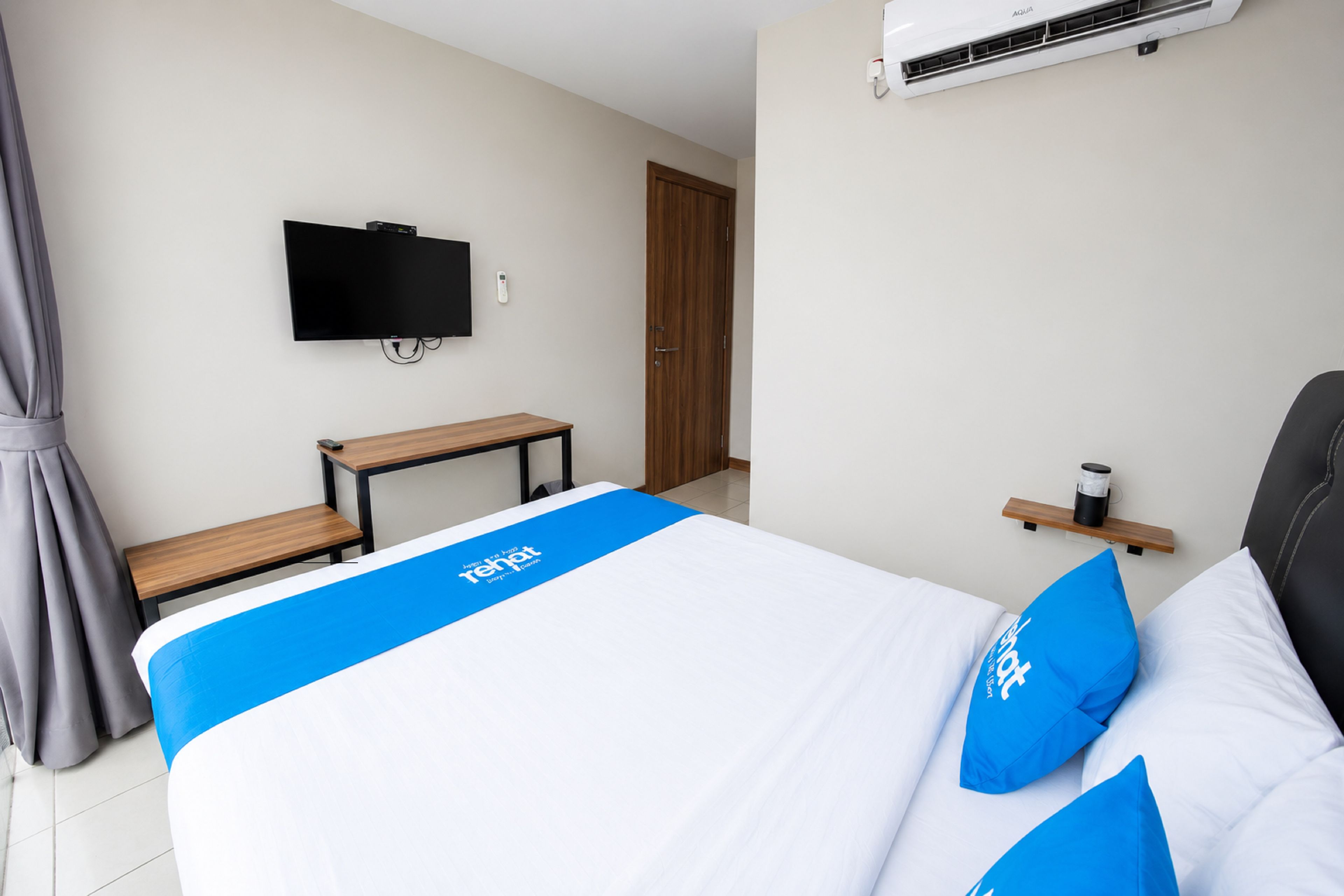 A hotel room with a bed, a desk, a television, an air conditioning unit, and a door.