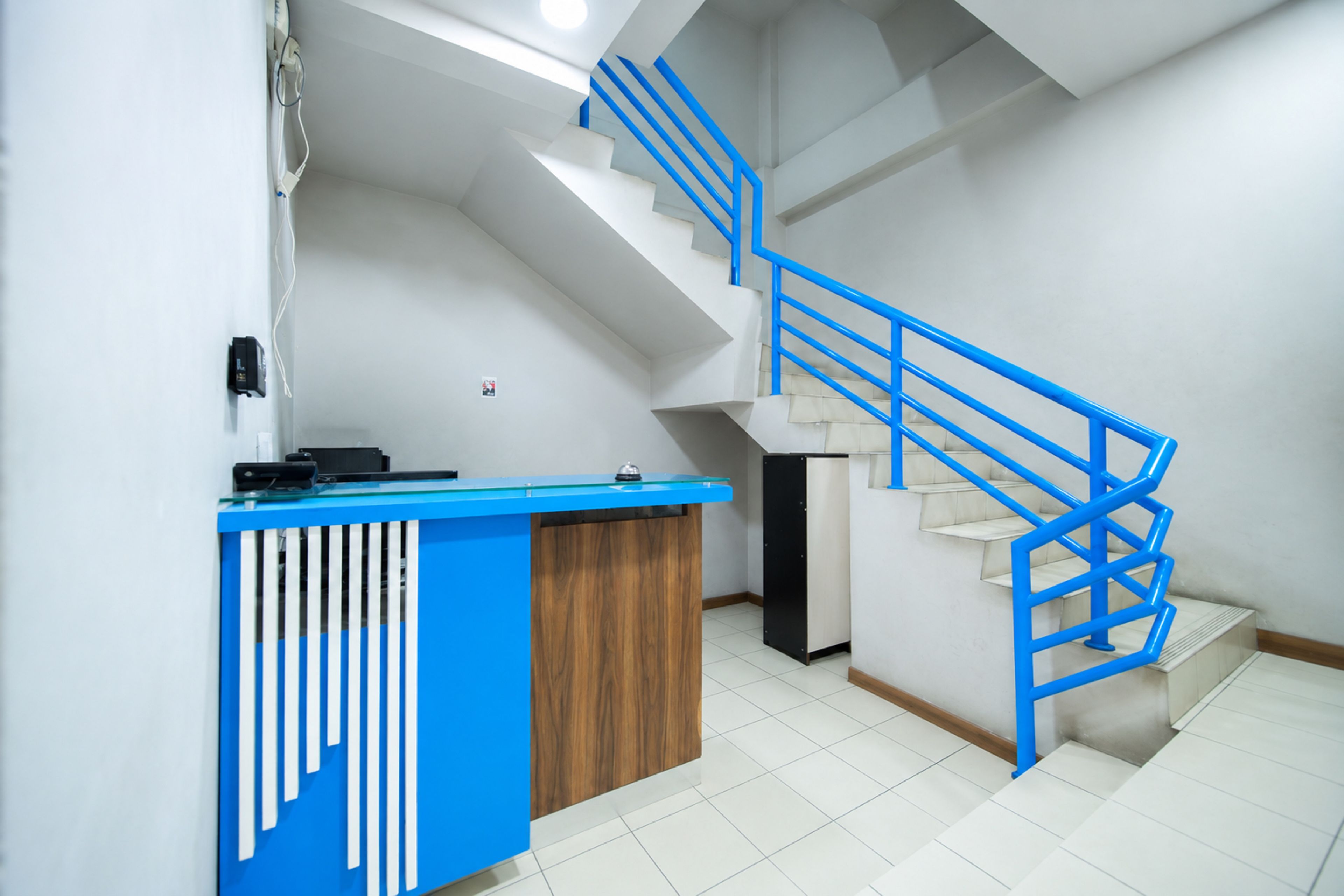 A reception desk with a blue and white design, a staircase with blue railings, and a tiled floor.