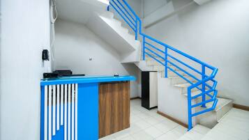 A reception desk with a blue and white design, a staircase with blue railings, and a tiled floor.
