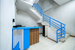 Un mostrador de recepción con diseño azul y blanco, una escalera con barandillas azules y un piso de baldosas.